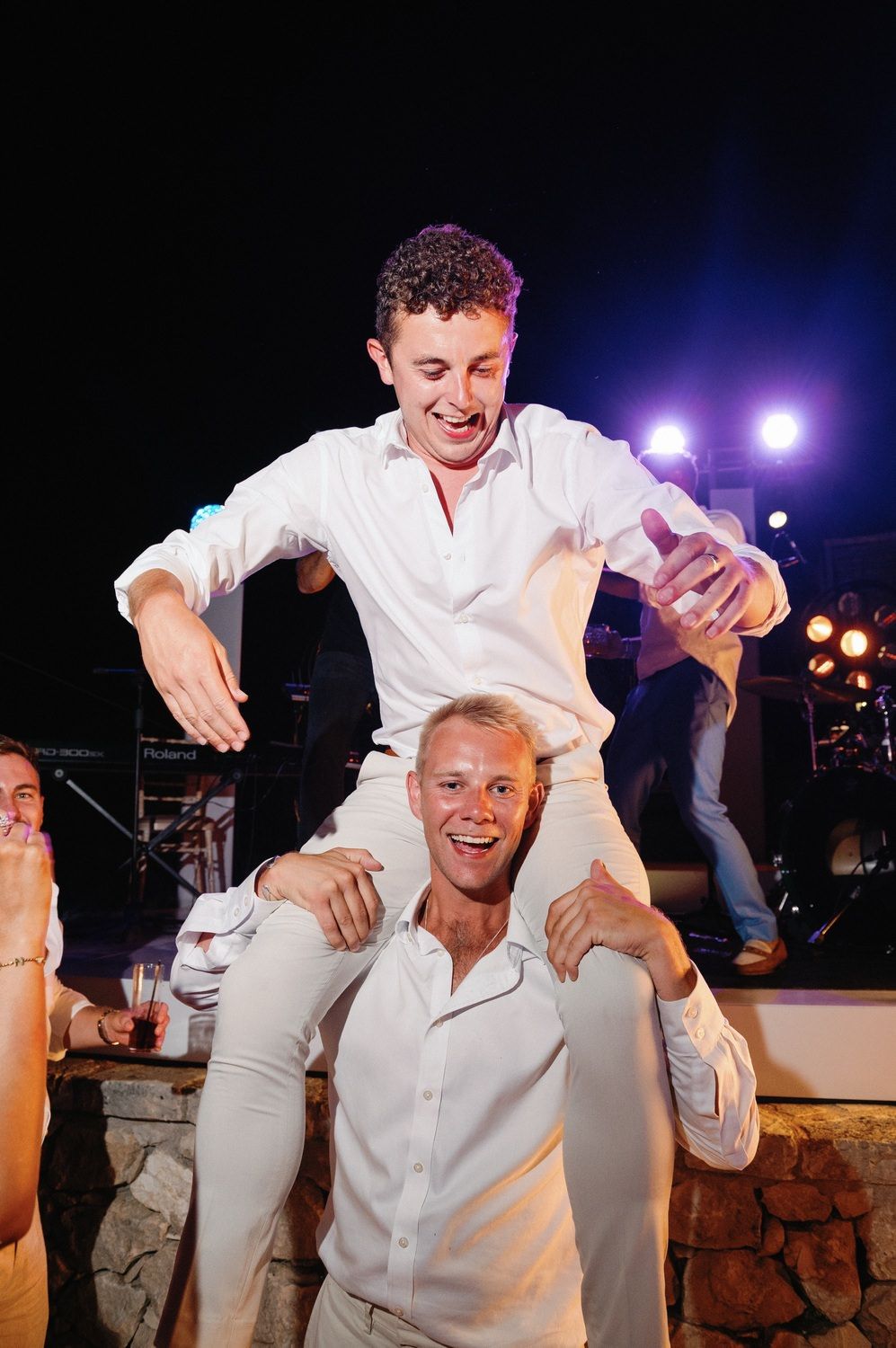 Two party guests in white shirts celebrating with playful shoulder ride during nighttime event.