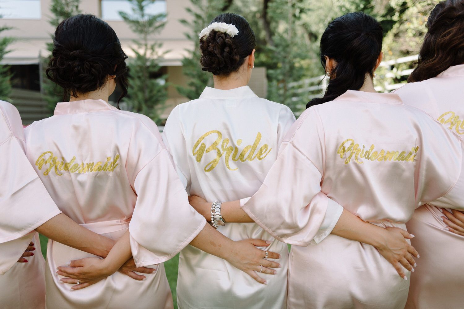 Back view of bridal party showing gold 'Bride' text on pink silk robes.