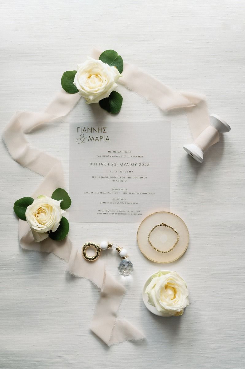Wedding invitation with white roses, silk ribbon, and rings styled on light background.