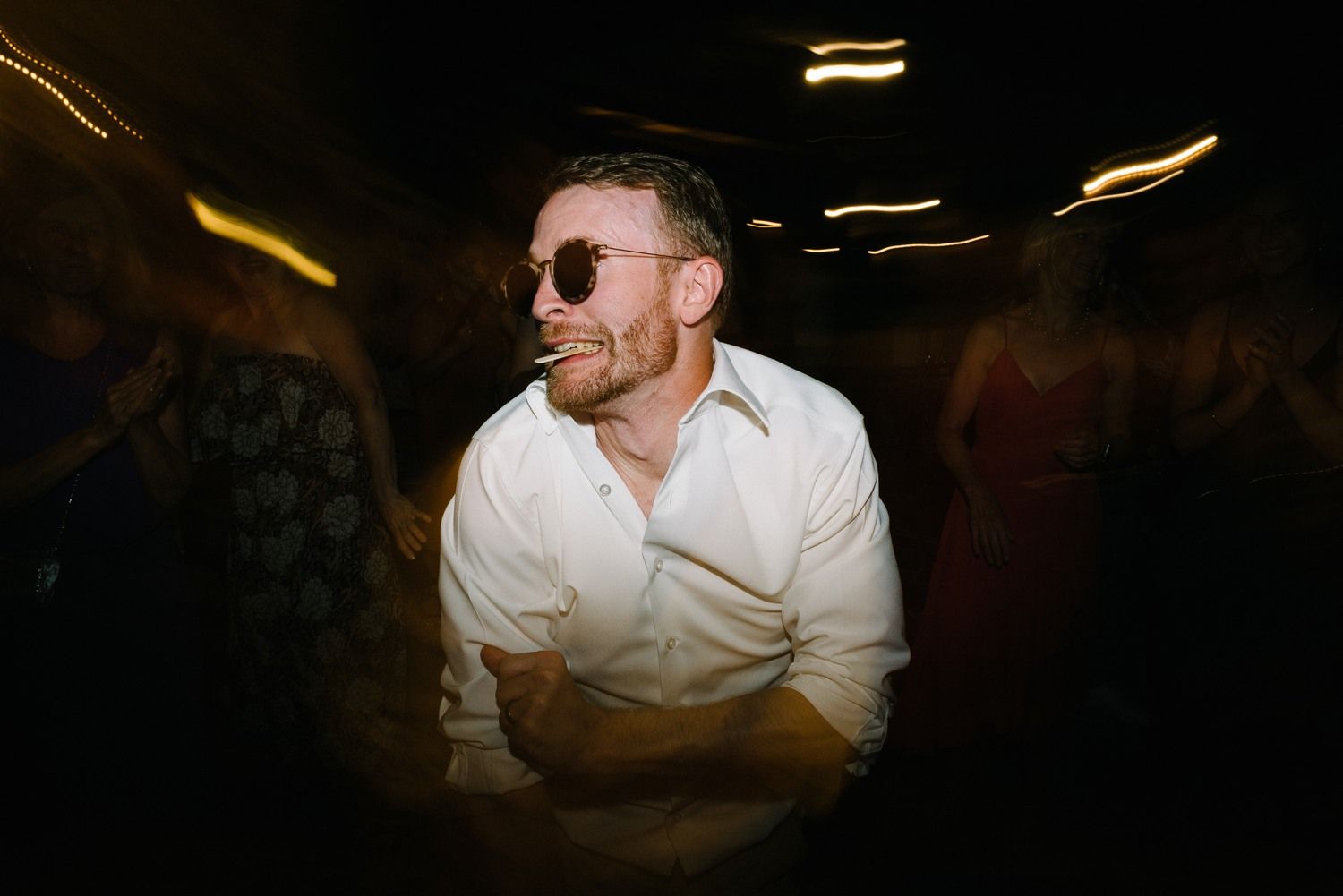 Stylish guest wearing sunglasses dancing in a dimly lit venue.