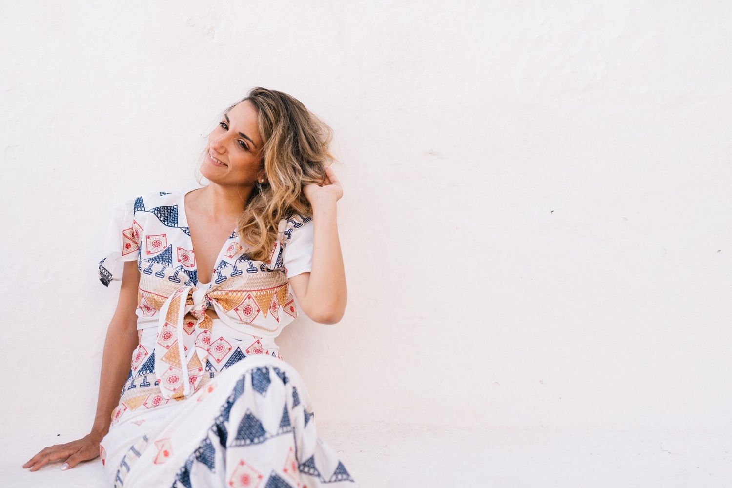 Woman in floral print dress poses against white wall during outdoor photoshoot.