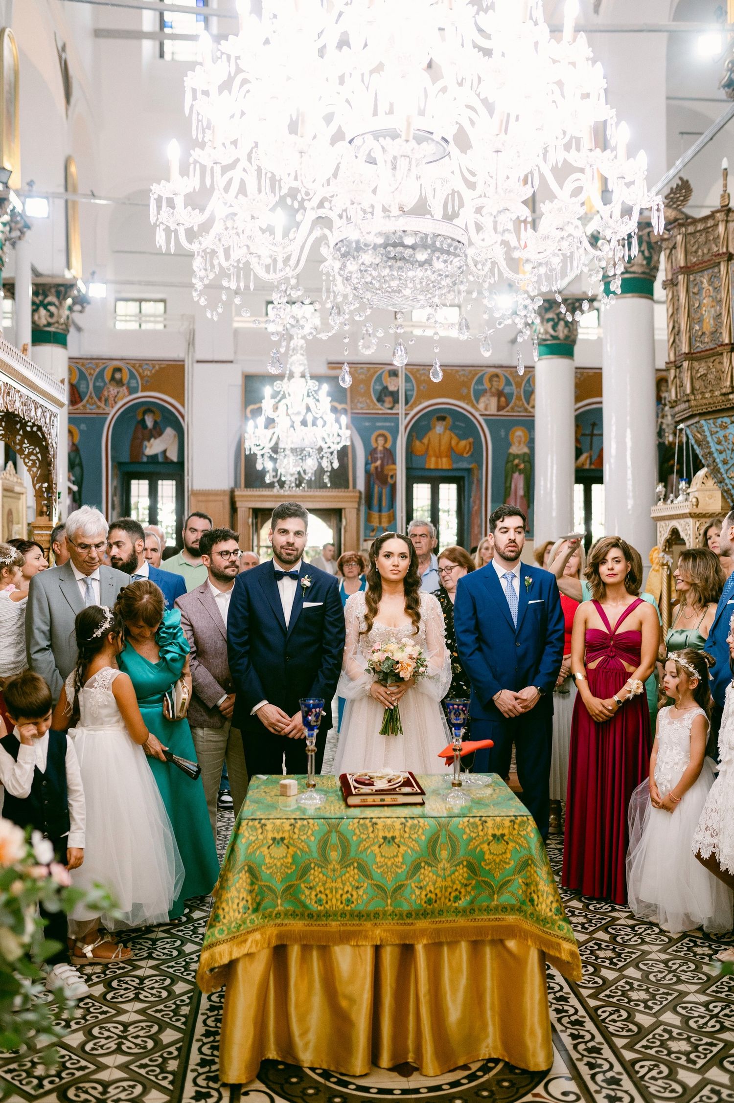 Elegant Orthodox church wedding ceremony with ornate chandelier and decorative green and gold altar table.