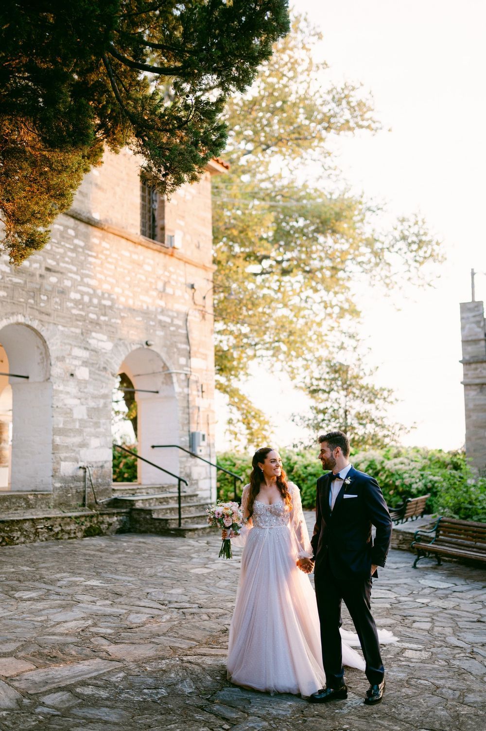 Couple shares a romantic moment on stone patio outside historic building during wedding photoshoot.