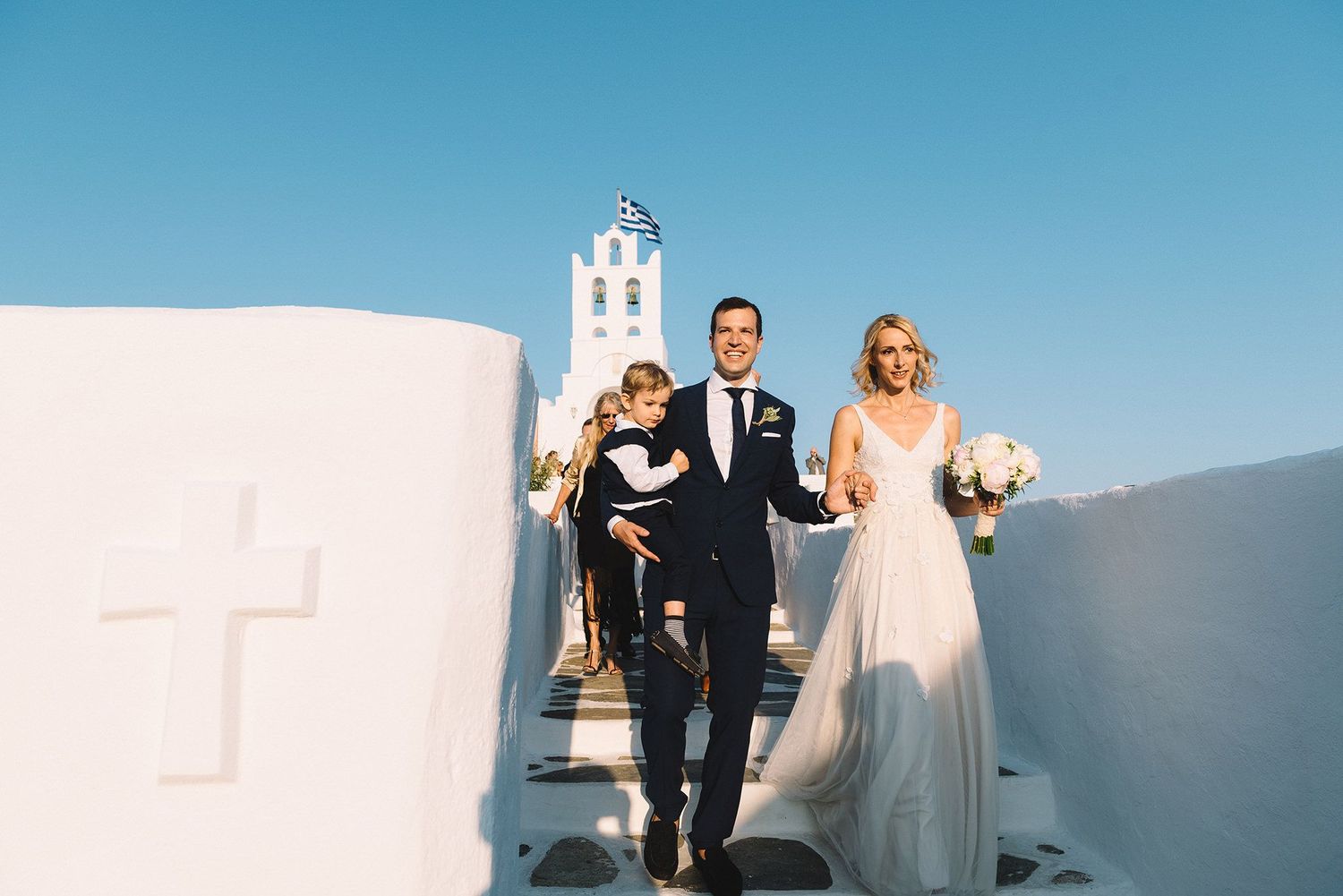 Wedding party walks along scenic white stone path overlooking Mediterranean Sea and blue sky in Sifnos island.