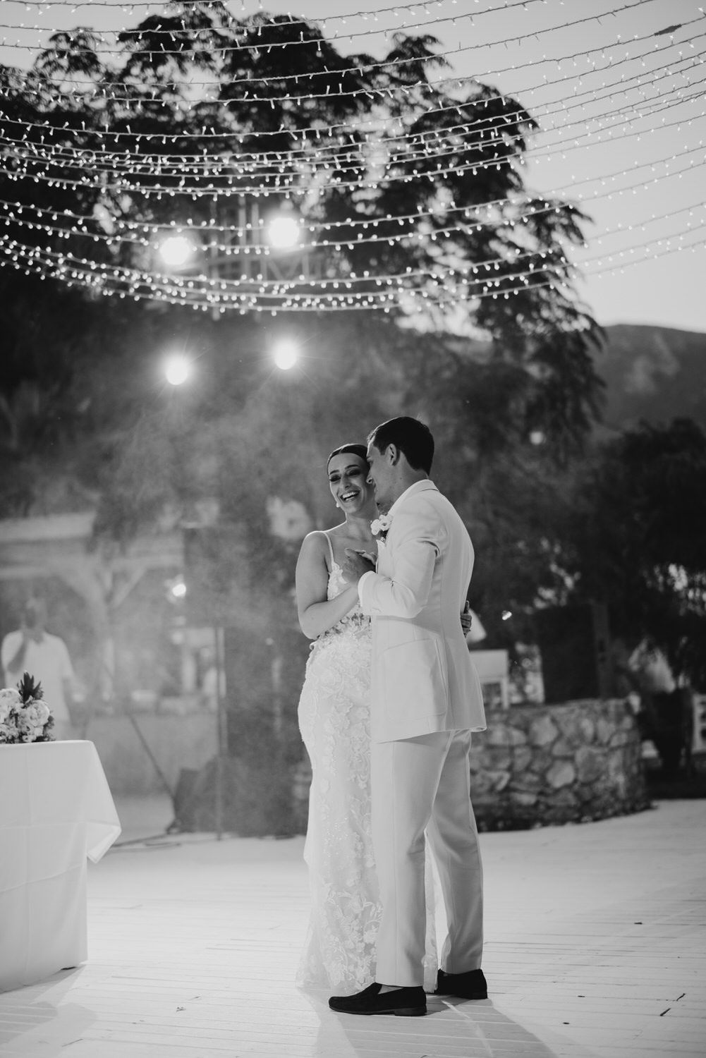 Elegant couple shares an intimate dance moment under a canopy of string lights at dusk.