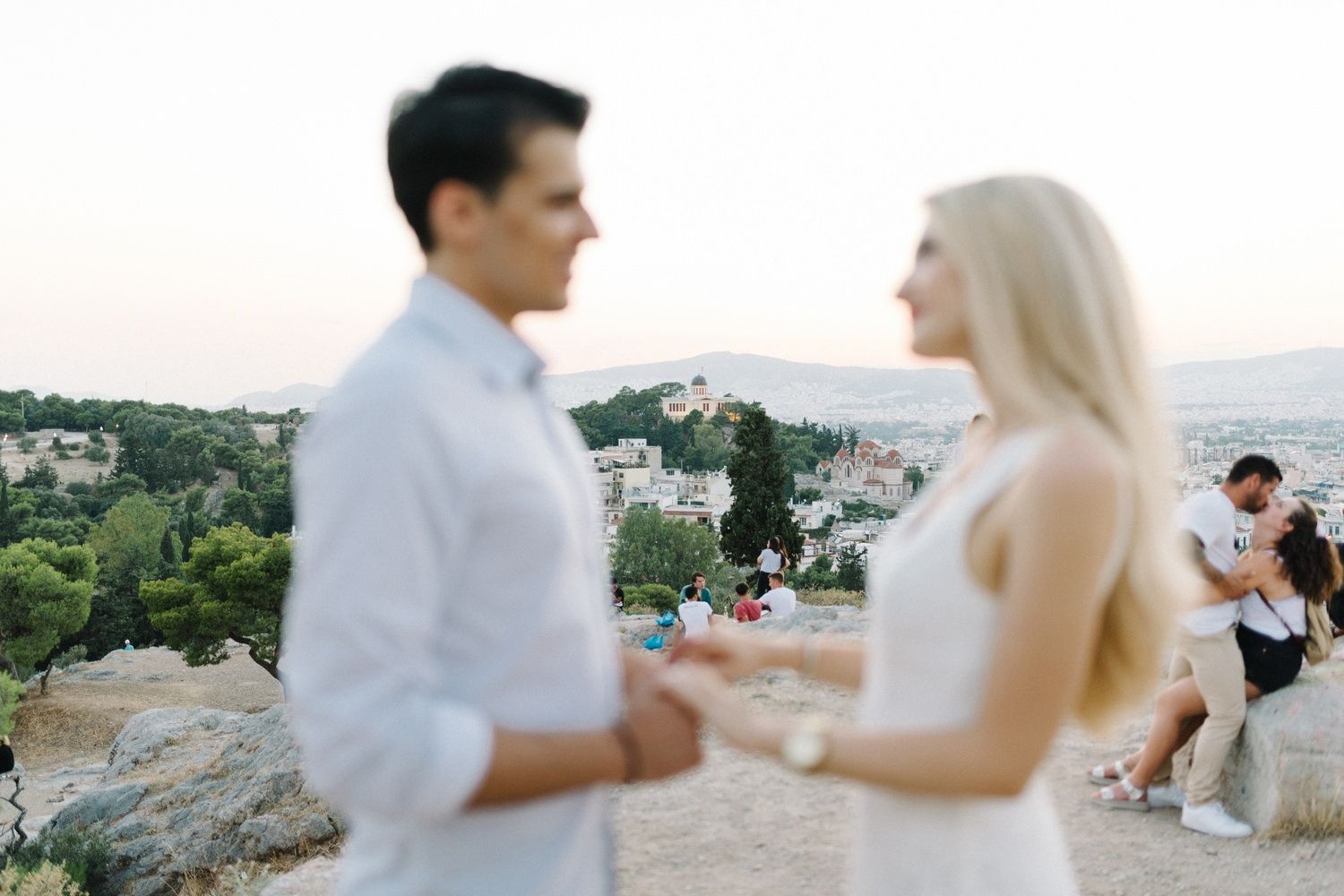 Couple sharing an intimate moment on a hilltop overlooking Athens at sunset.