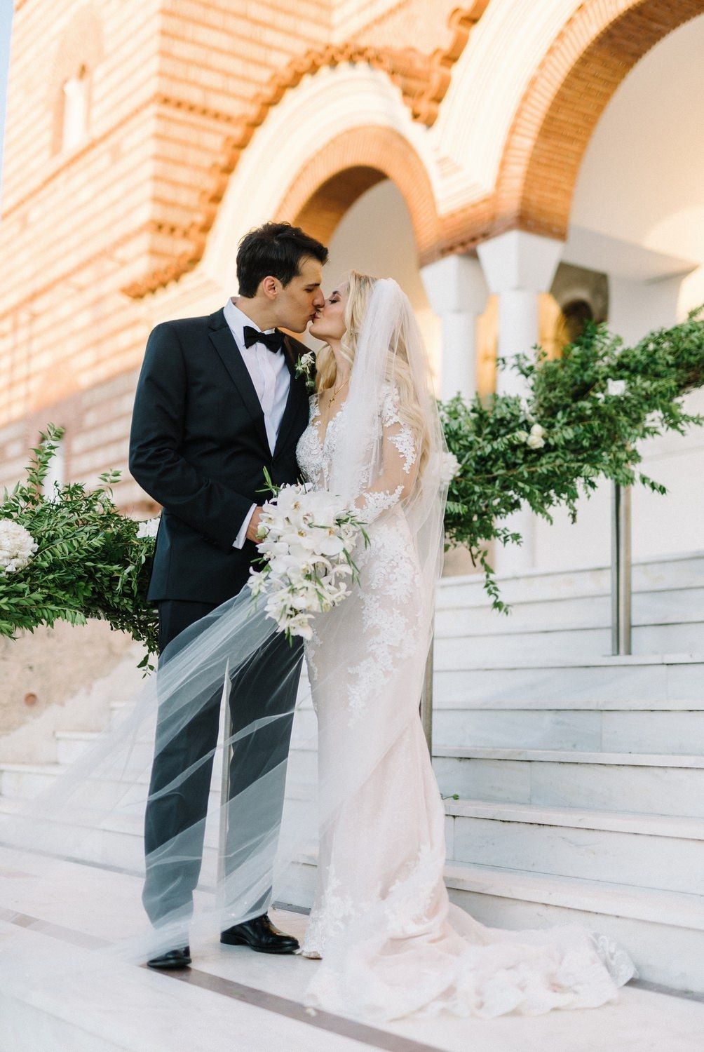 Romantic wedding couple sharing an intimate moment on marble steps under ornate Mediterranean arches.