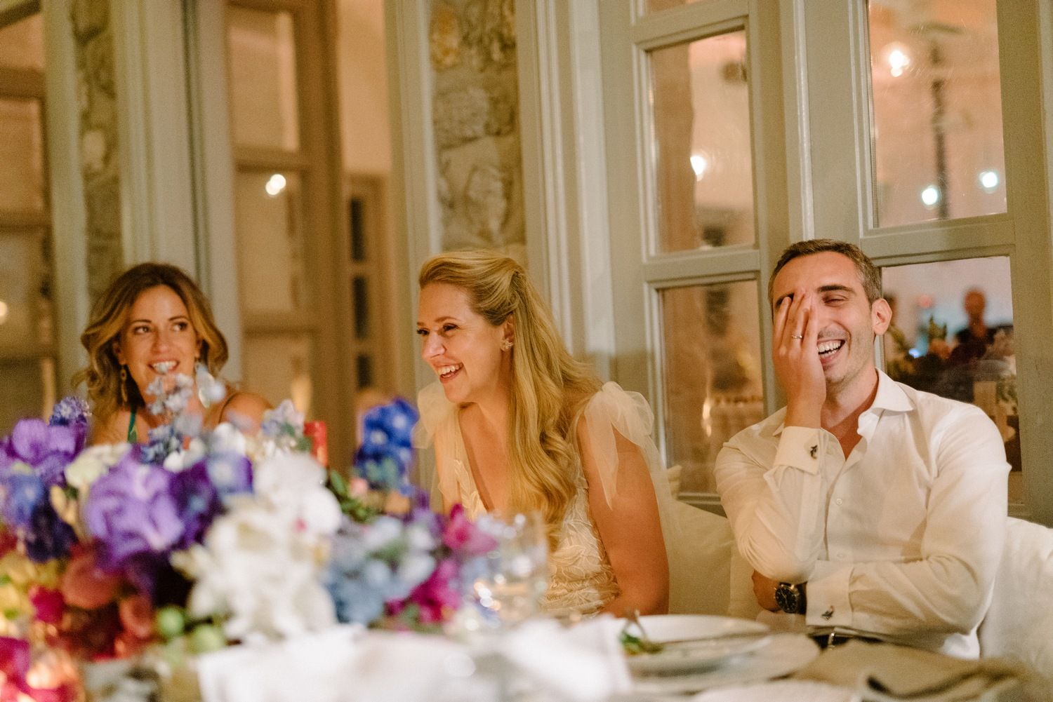 Wedding reception moment with guests reacting to speeches at an elegant dinner setting.