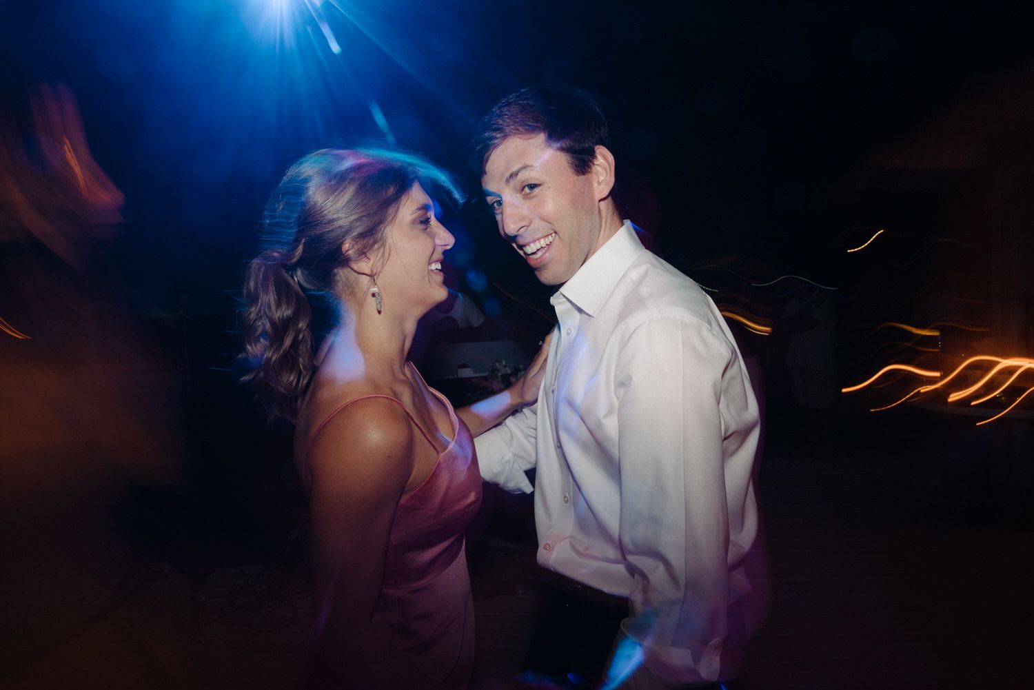 Wedding guests dancing under blue spotlights at an evening reception.