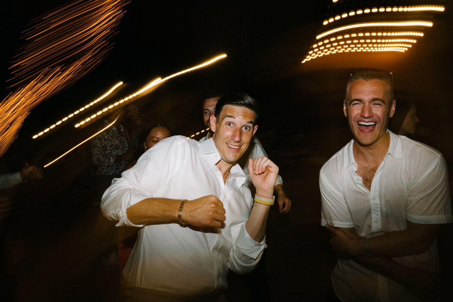 Two party guests posing and gesturing with light trails in the background.