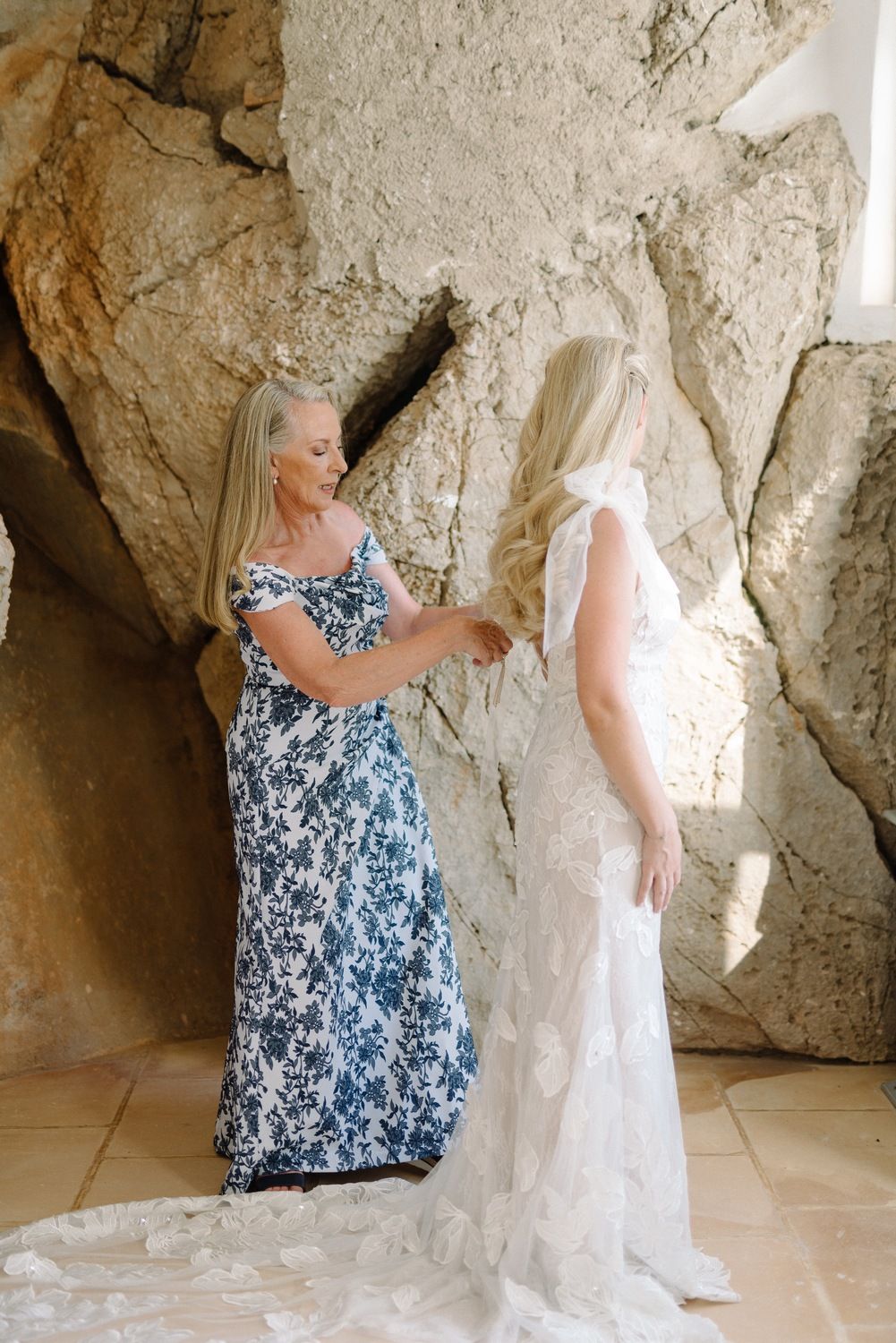 Wedding dress fitting moment against rustic stone wall backdrop.