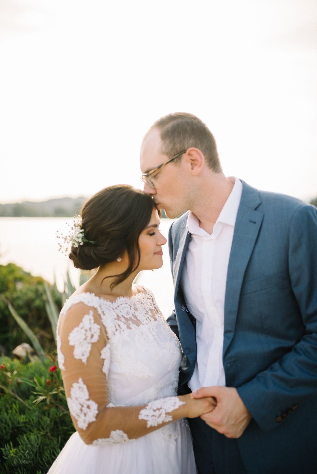 Intimate moment between newlyweds against coastal background.