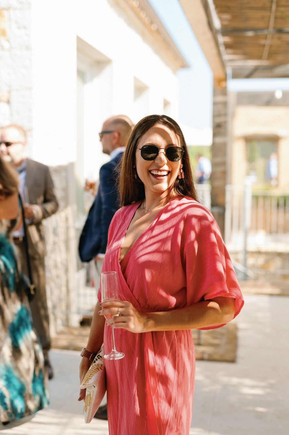 Wedding guest in coral dress holding champagne at outdoor reception.