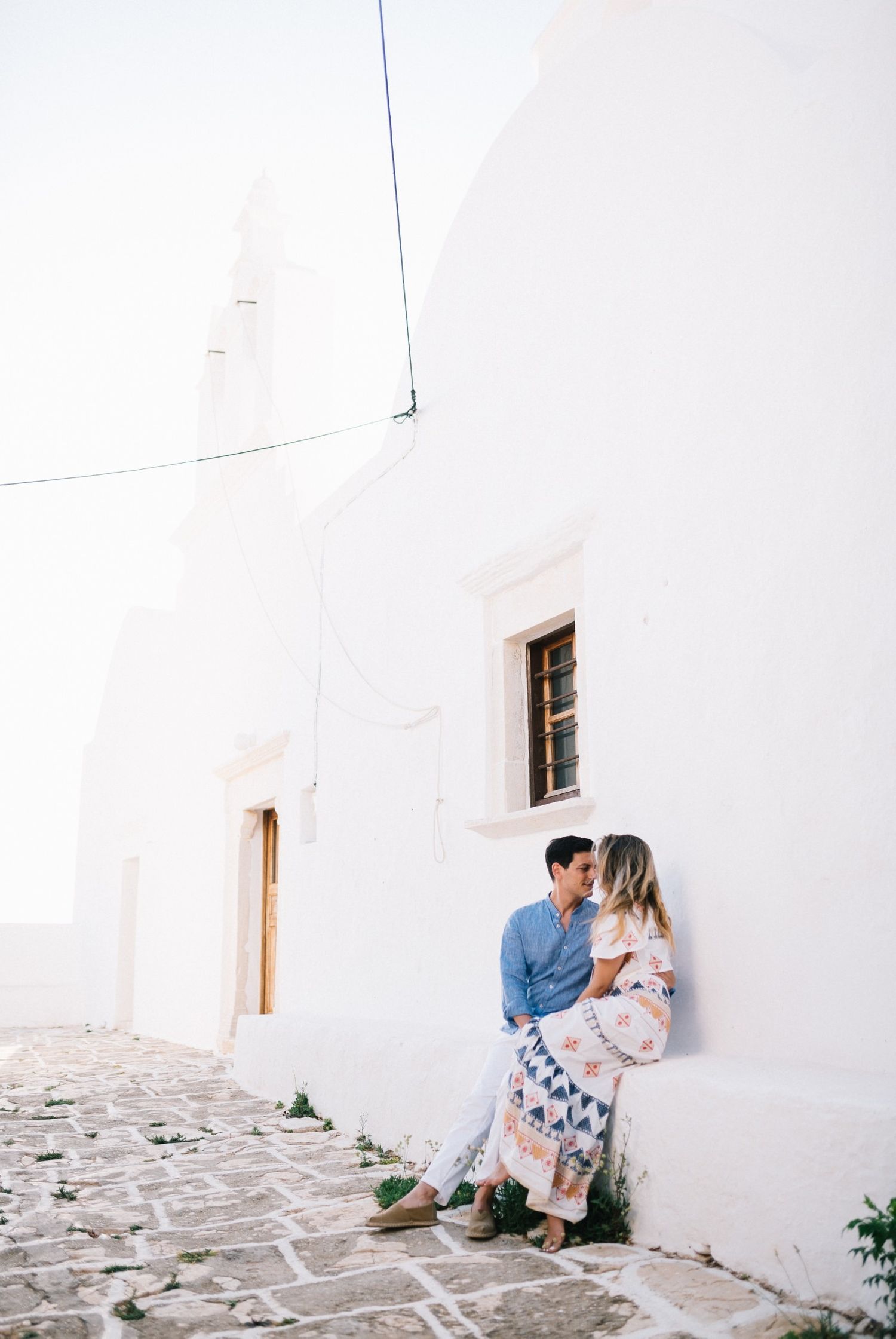 A couple sharing an intimate moment against a pristine white building wall with cobblestone path.
