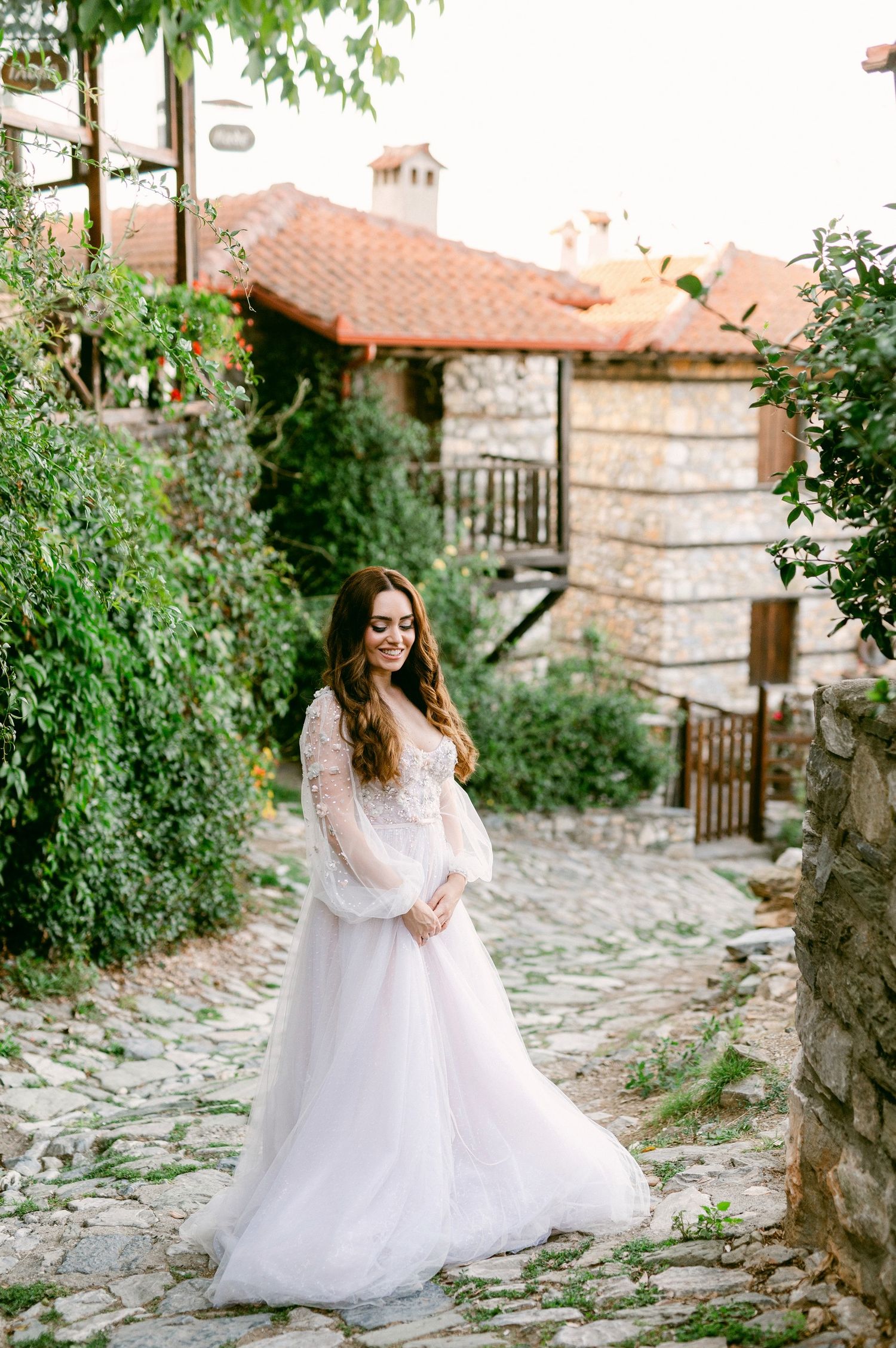 A flowing white wedding gown creates an ethereal scene against a rustic stone path and Mediterranean-style villa backdrop.