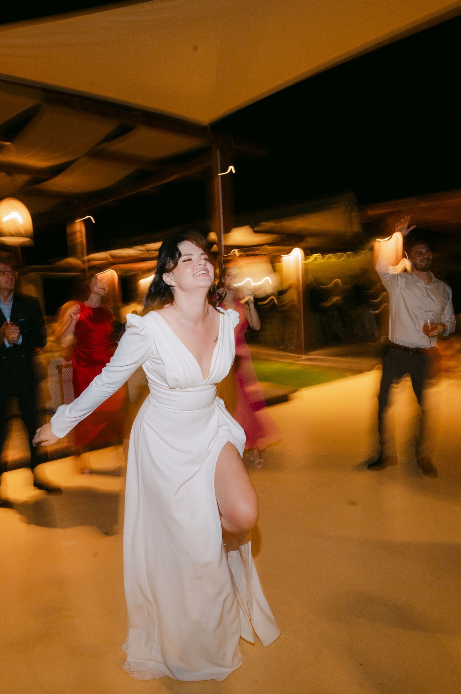 Motion blur captures dancers in white attire spinning and moving across a dimly lit indoor dance floor.
