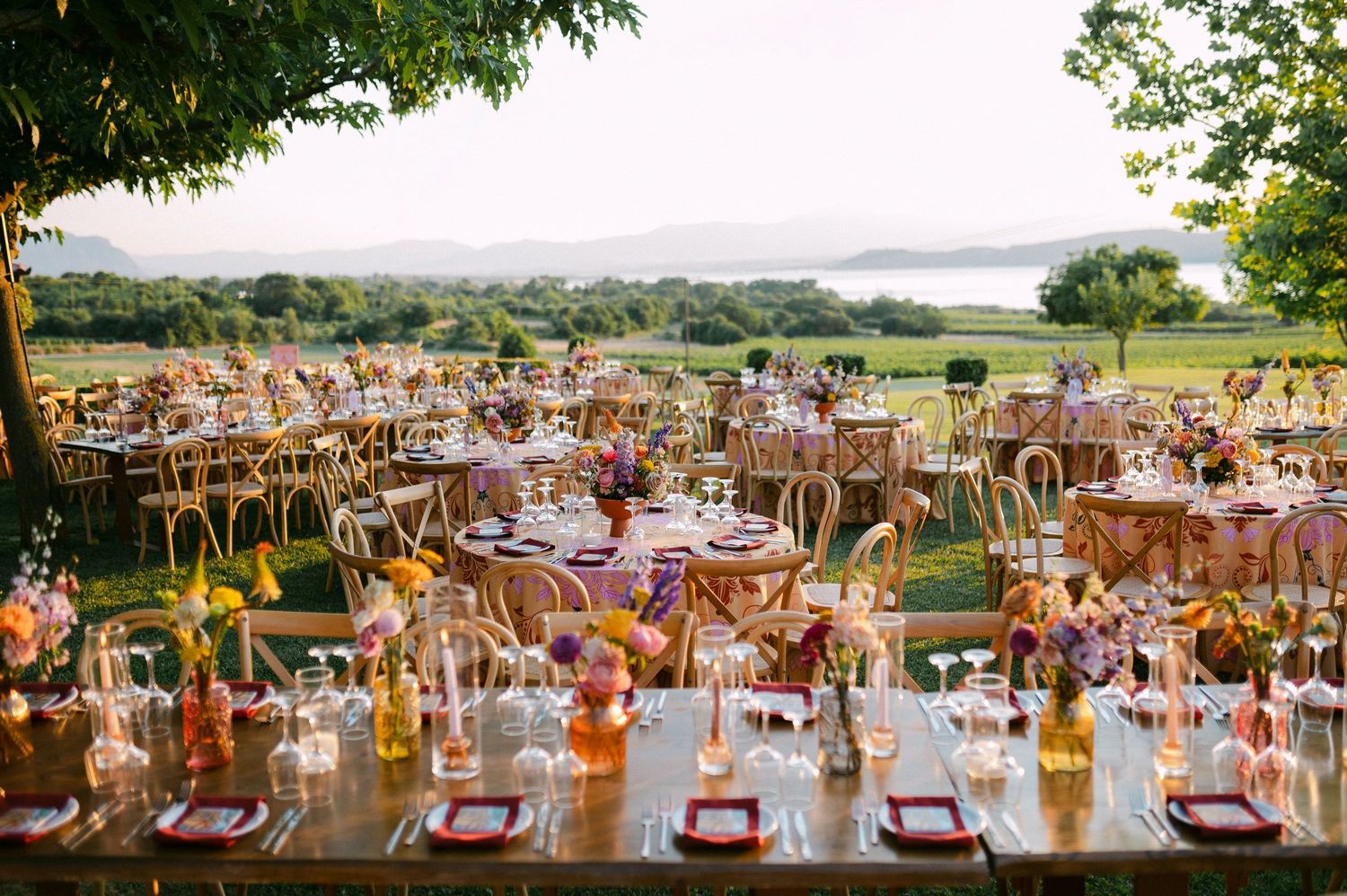 Elegant outdoor wedding reception tables arranged under string lights with scenic countryside views in background in vineyard Kamkoutis