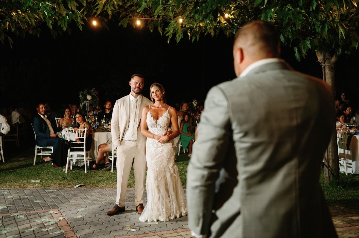 Wedding couple poses for photos under string lights at outdoor garden reception.