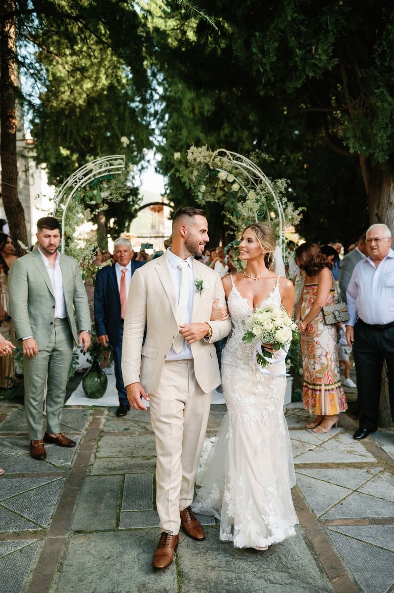 Wedding couple walking down stone pathway under decorative floral arch.