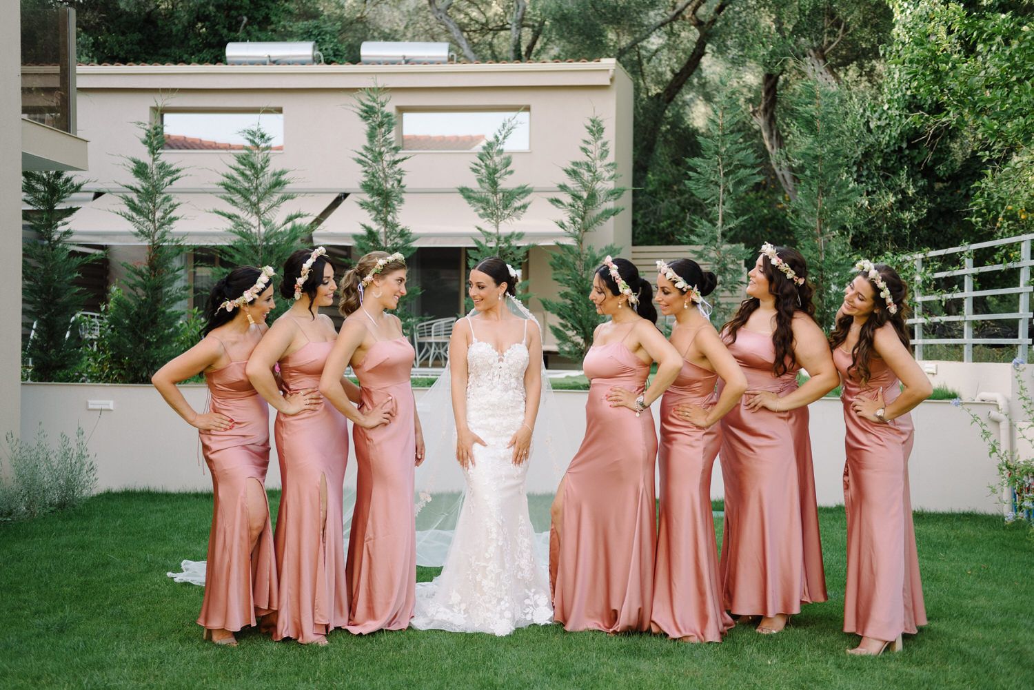 Wedding party portrait with bridesmaids wearing matching pink gowns posing in a garden setting.