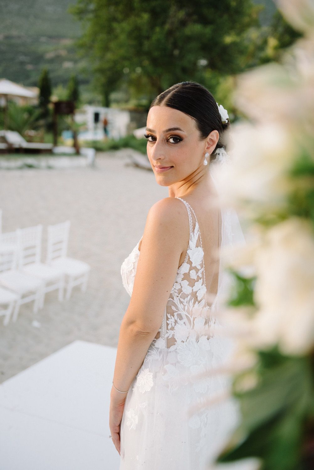 Bride in elegant lace wedding dress poses at outdoor venue.
