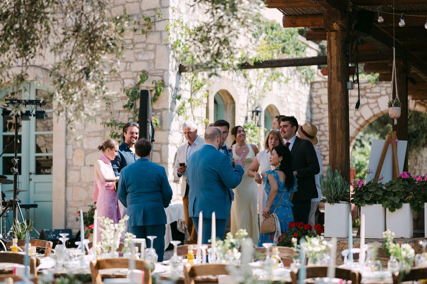 Guests mingle at an elegant outdoor wedding reception under string lights at a rustic stone venue.