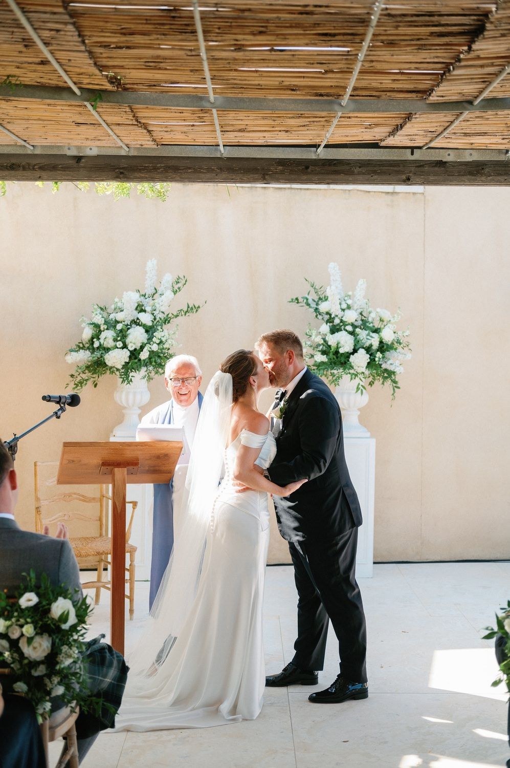 Wedding ceremony moment with white floral arrangements and an officiant at a podium.