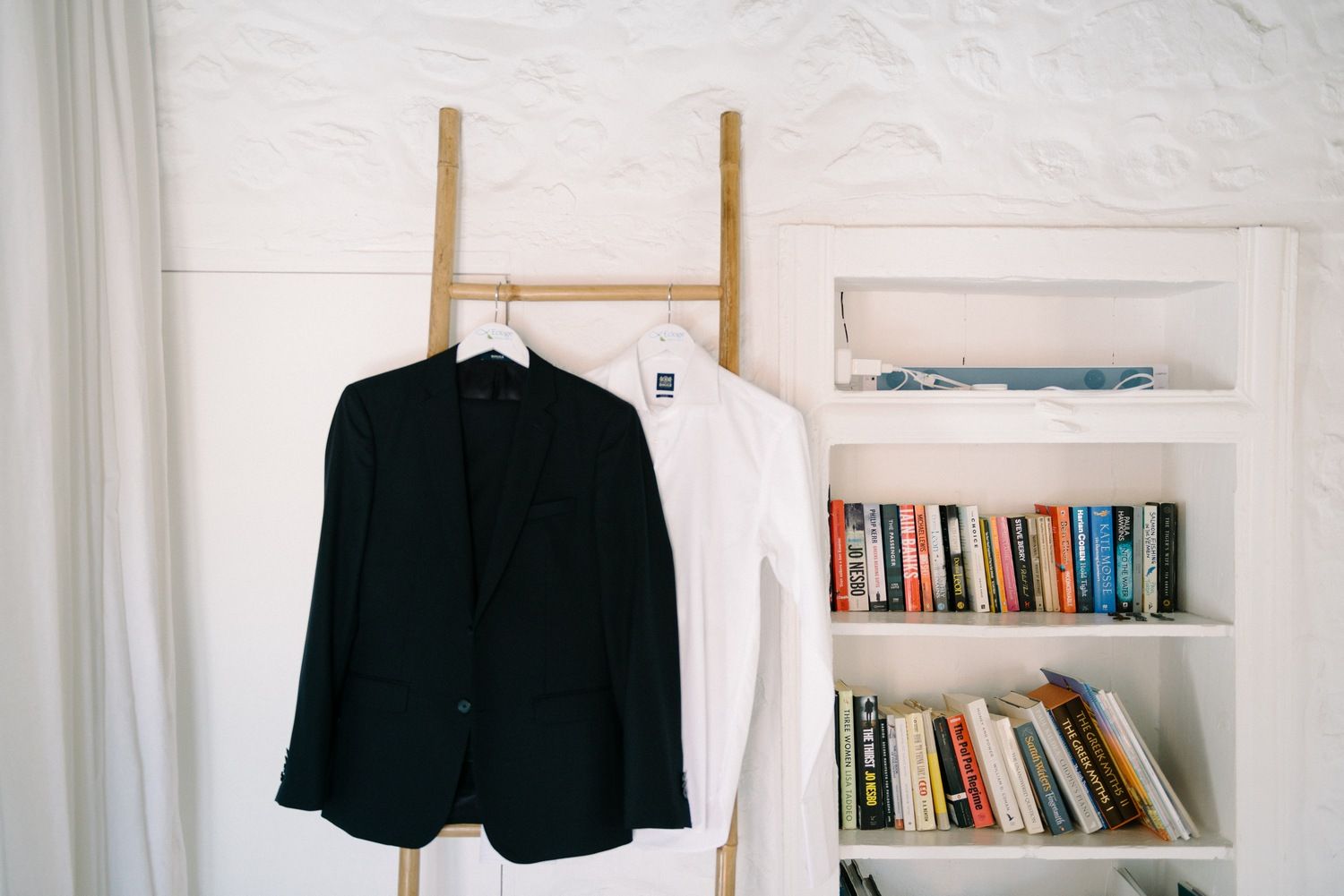 Black and white blazers hanging on wooden ladder next to bookshelf.