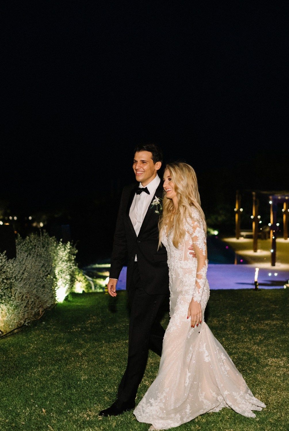 Elegant couple poses for nighttime wedding portrait on illuminated lawn.