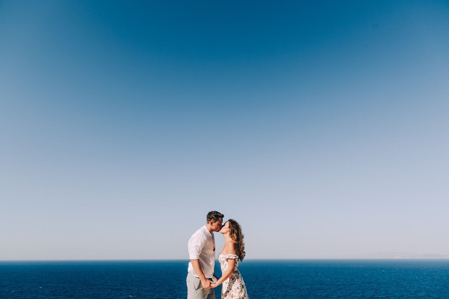 Intimate moment between couple against minimalist blue sky and ocean background.