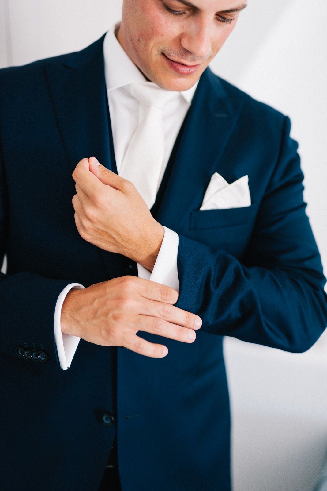 Close-up of a navy blue suit jacket with white pocket square and cufflink adjustment.