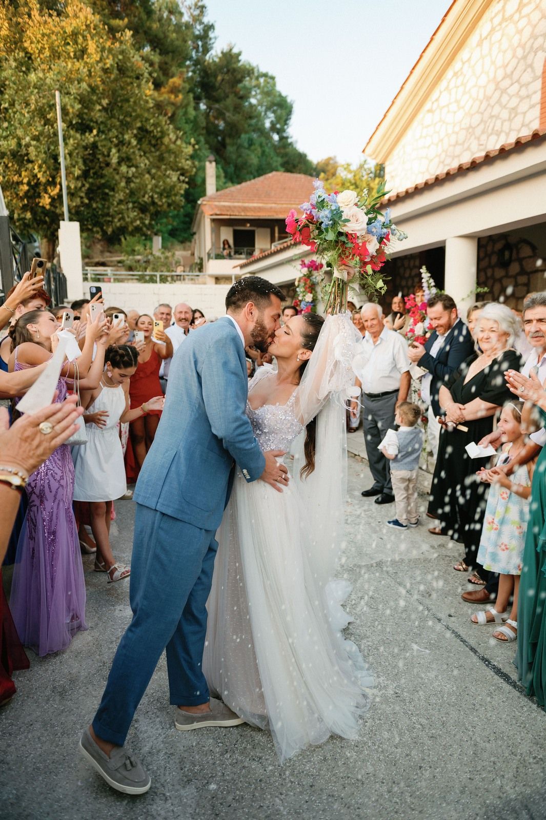 Wedding celebration with guests throwing confetti as couple shares romantic moment outside venue.