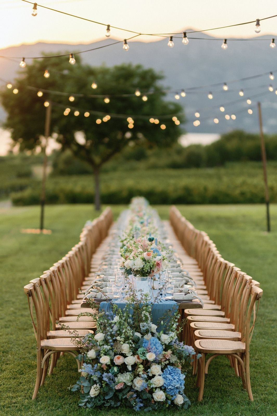 Outdoor wedding reception setup with wooden chairs and blue floral centerpieces in vineyard Kamkoutis at Velventos, Greece