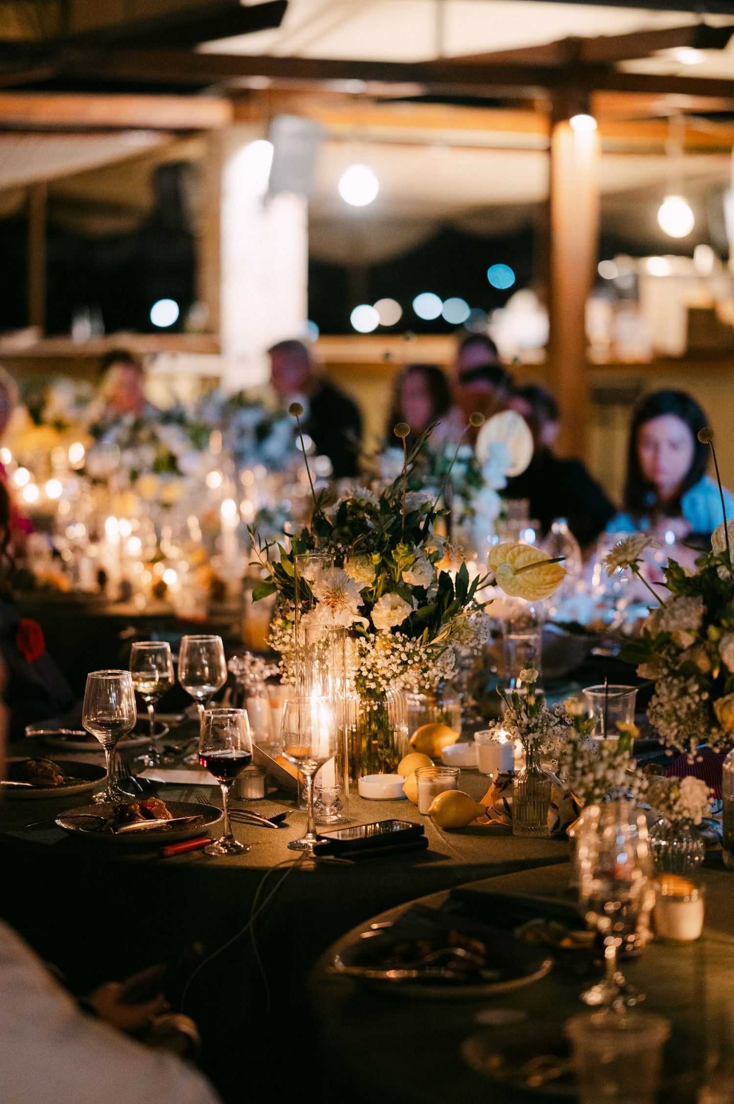 Elegant wedding reception tables decorated with candlelit mason jars and floral arrangements in a dimly lit venue.