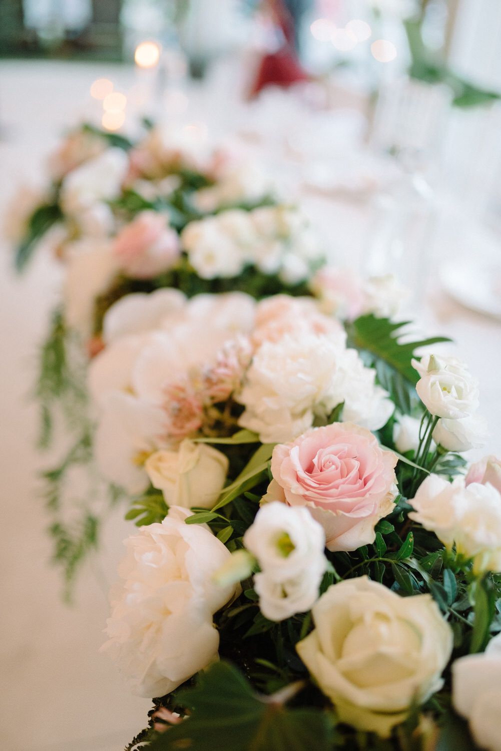 Romantic floral centerpiece with pink and white roses arranged along wedding reception table.