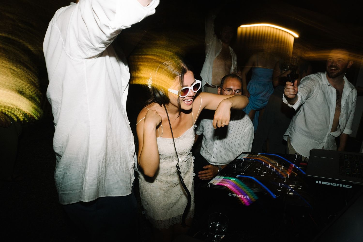 Guests dance and party near DJ equipment at a wedding reception.