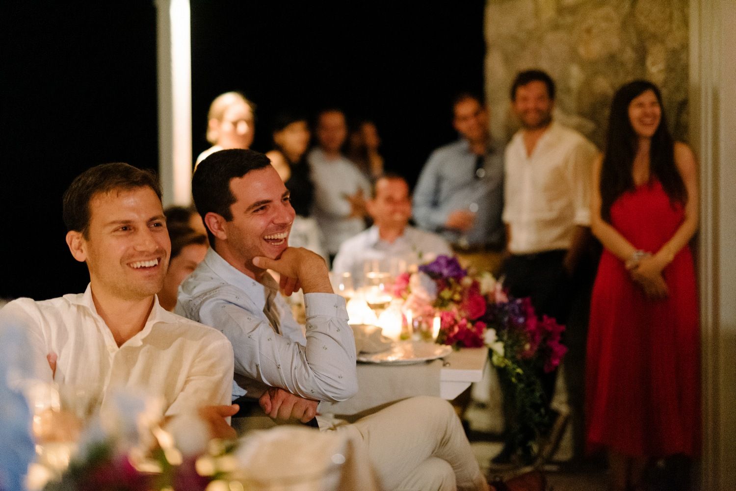 Evening wedding reception with guests seated at candlelit tables with floral arrangements.