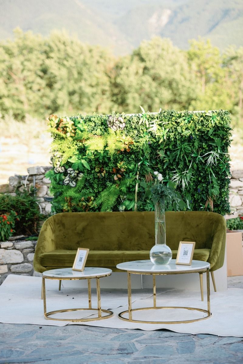 Modern lounge area featuring velvet green sofa and gold accent tables against living plant wall.