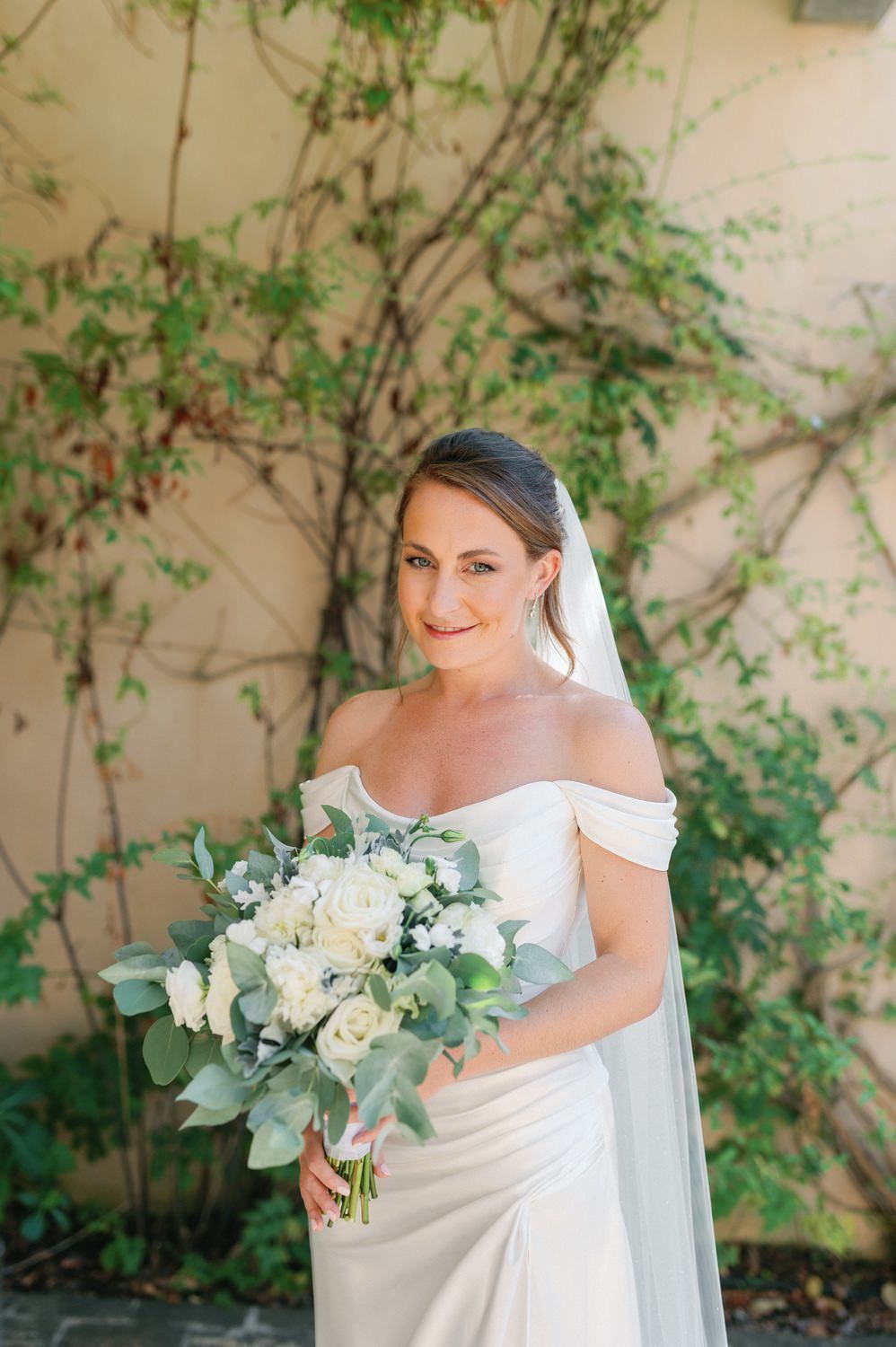 A bridal portrait showcasing a white floral bouquet against a backdrop of climbing greenery.