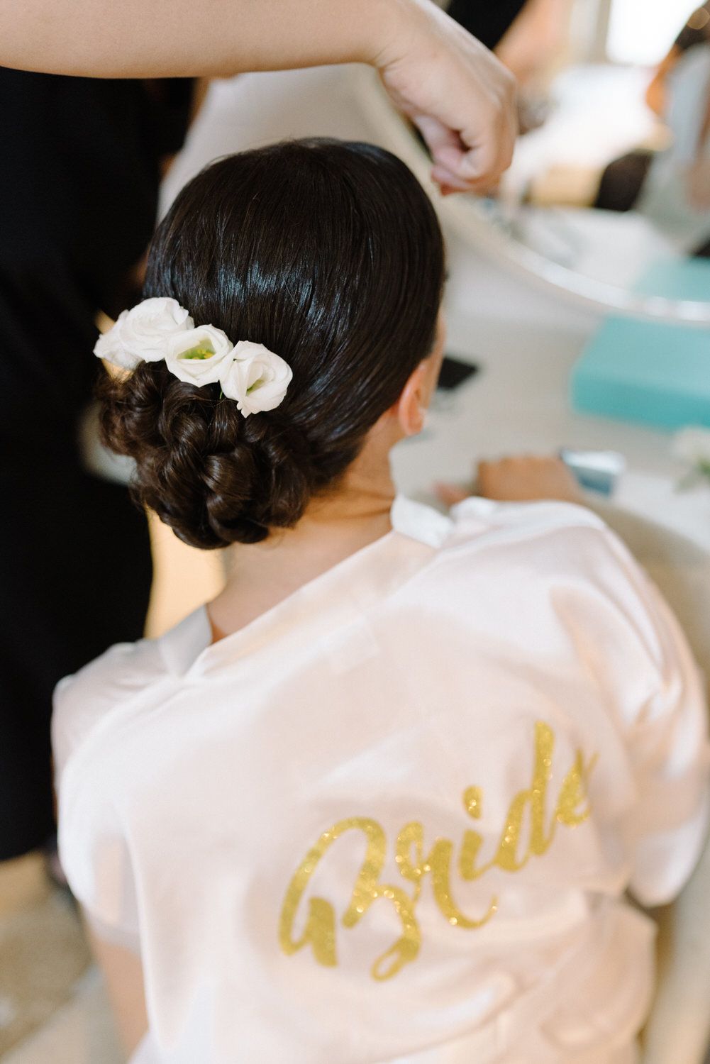 Elegant bridal hairstyle with white flowers and gold 'Bride' text on robe.