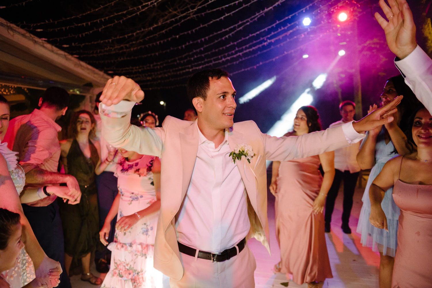 Wedding reception dance party with colorful lighting and guests in pink attire.