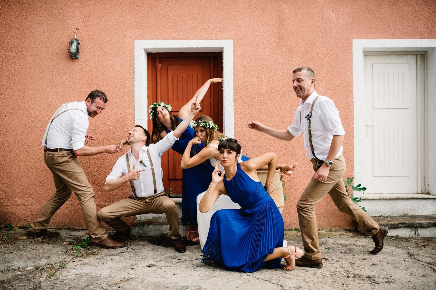 Wedding party striking dramatic poses in front of a coral building entrance.