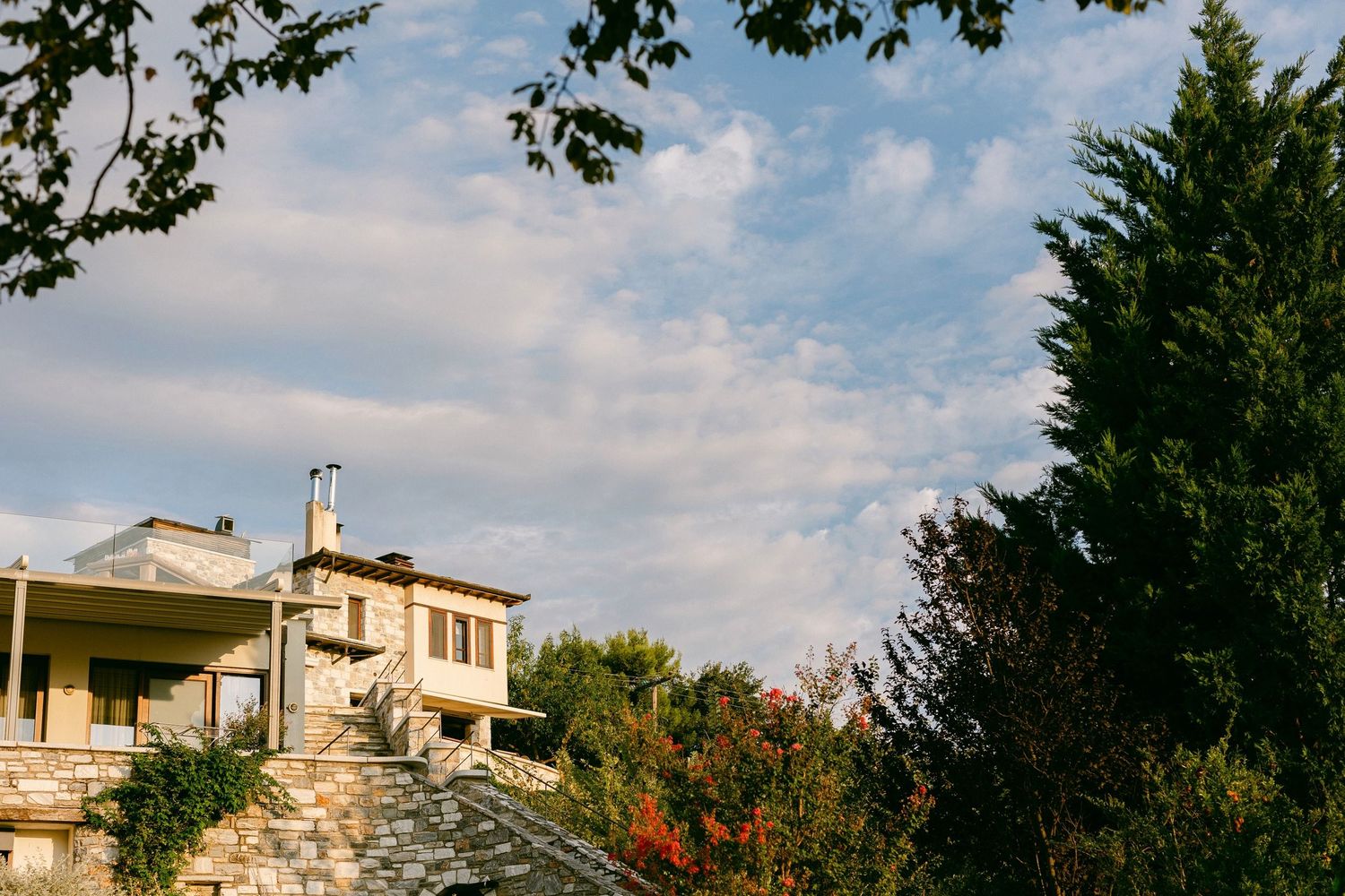 A Mediterranean-style villa perched on a hillside with autumn trees and cloudy skies in the background.