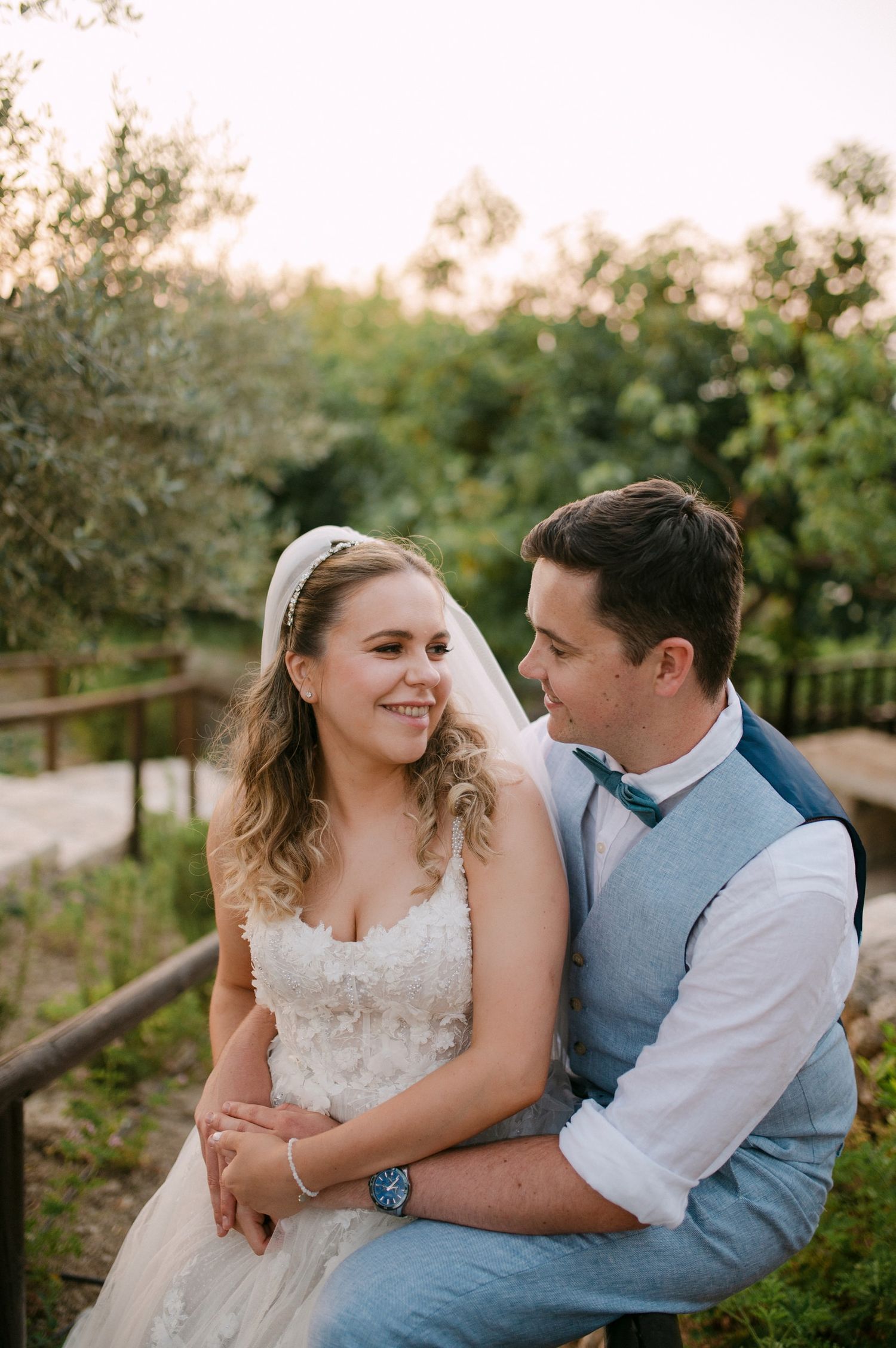 A newly married couple embrace outdoors in a garden setting during their wedding photo session.