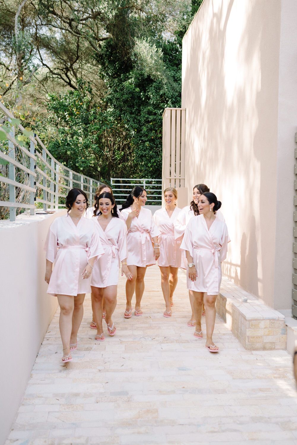 Bridal party walking together in pink robes along an outdoor pathway.