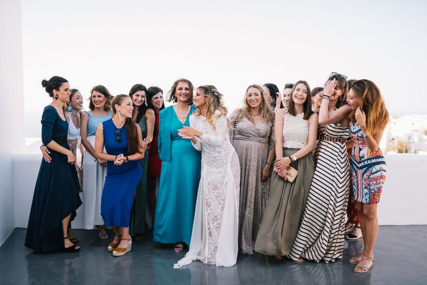 Wedding party in coordinated dresses posing together against white wall backdrop.