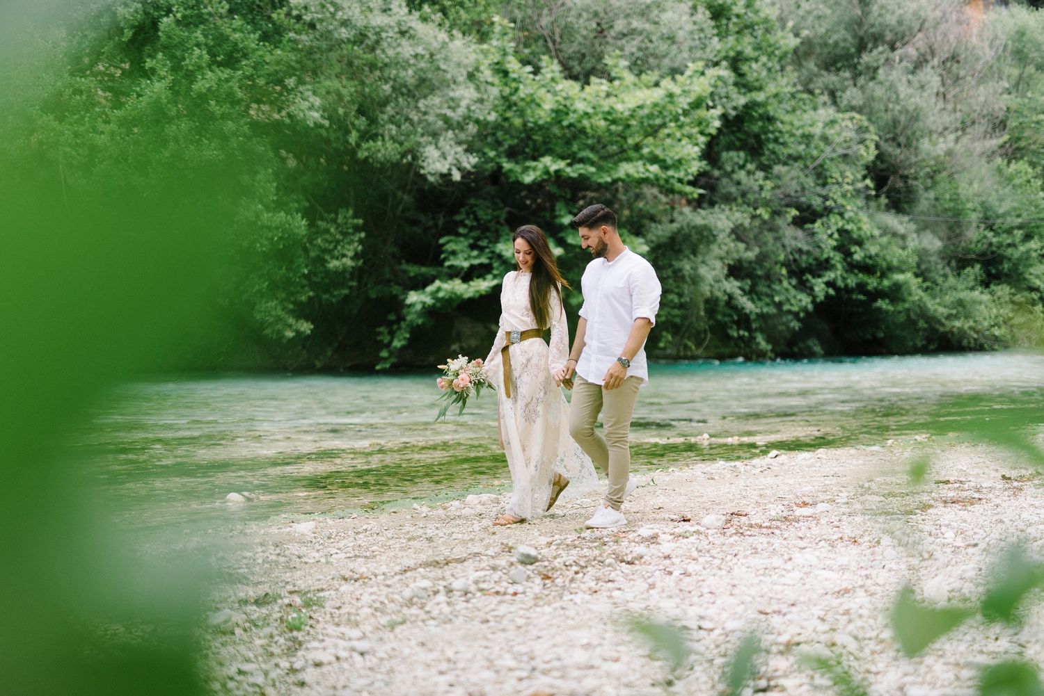 Couple walking together on sandy path surrounded by green foliage.