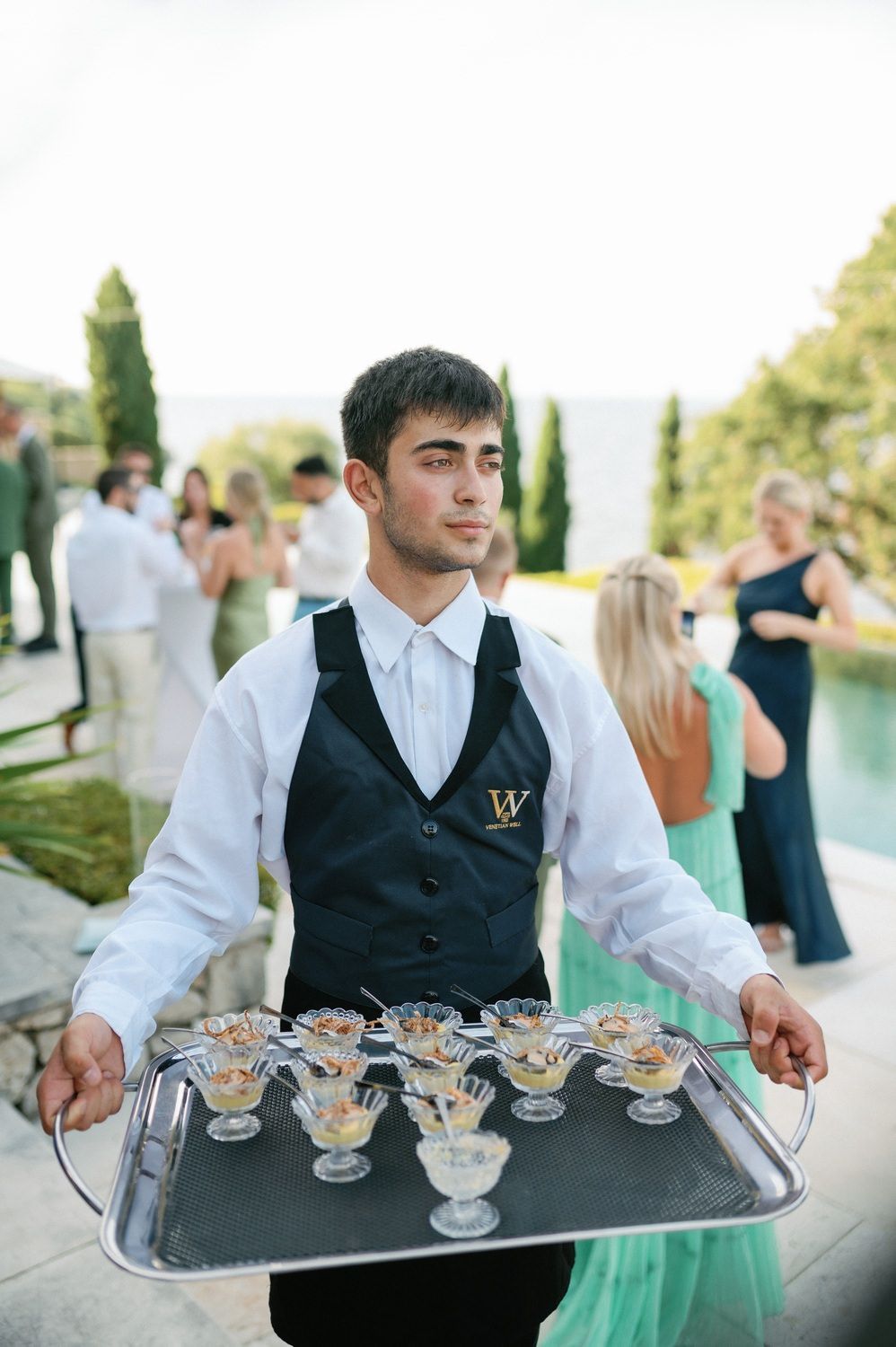 Server carrying tray of champagne glasses at an elegant outdoor wedding reception.