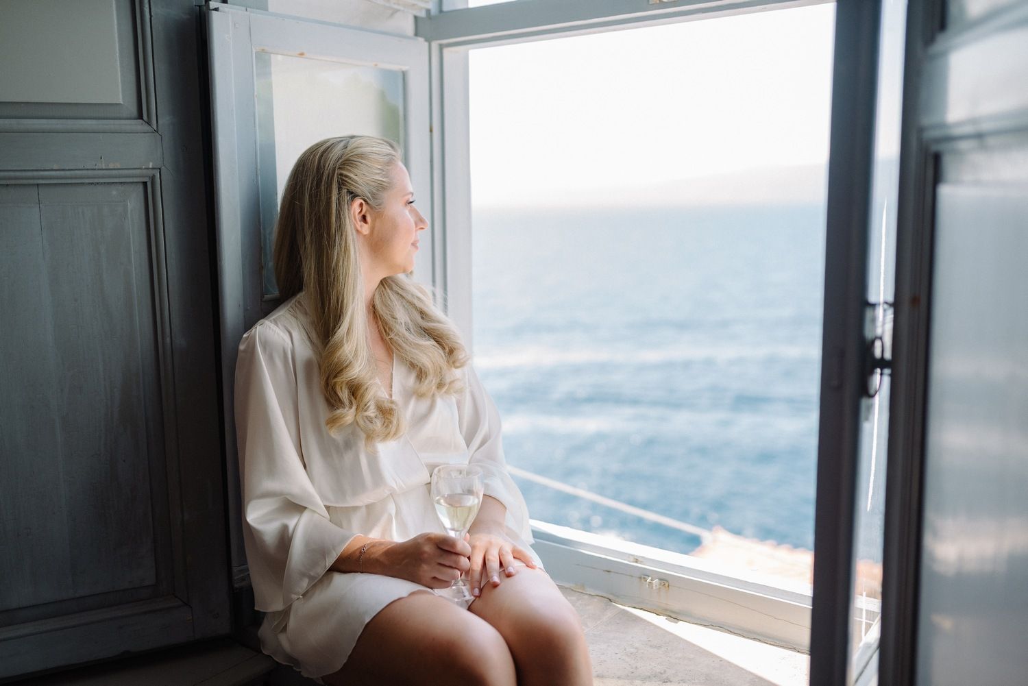 A person in a white shirt sits by a window overlooking the ocean.