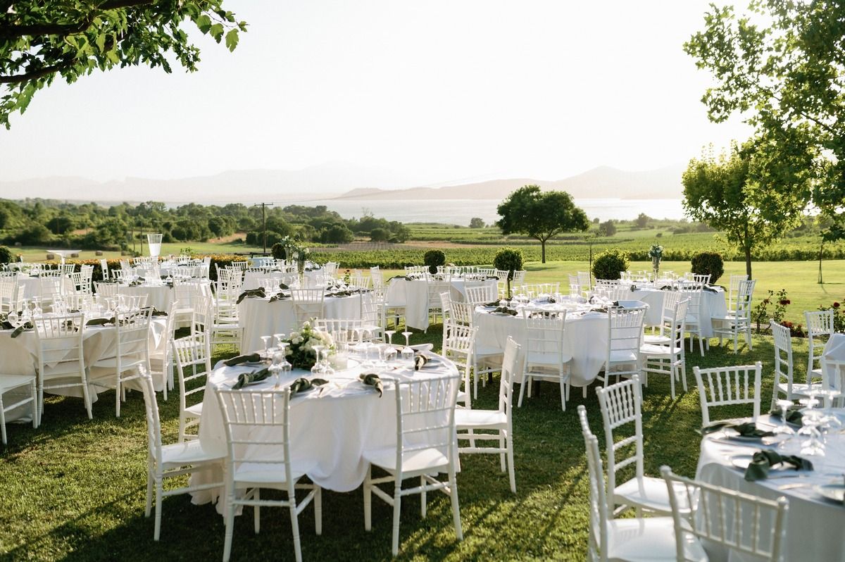 Outdoor wedding reception with white tables and chairs arranged on grassy hillside venue.